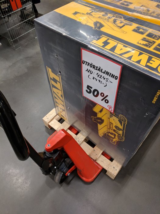 En DeWalt-produktpackning på en pall med en röd palltruck, försedd med en röd "Utförsäljning 50%" lapp.