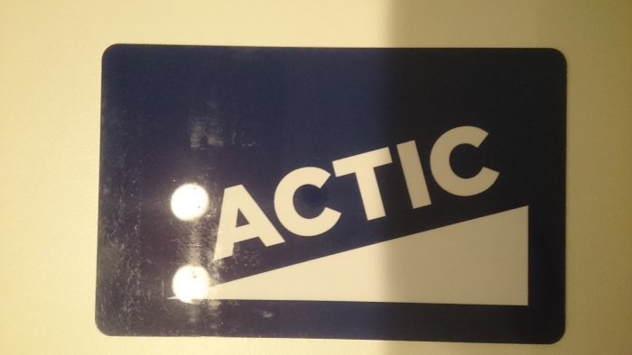 Skylt med texten "ACTIC" med två fästpunkter på en vägg.