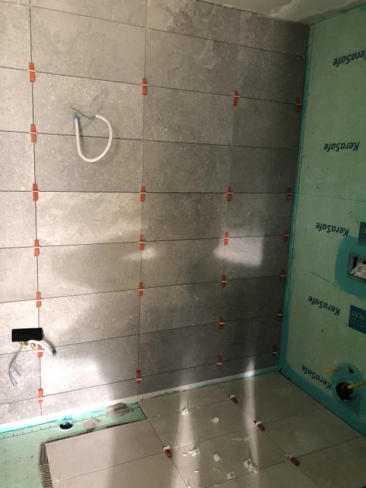 Omfattande badrumsrenovering med delvis lagda grå klinkerplattor och väggisolering.