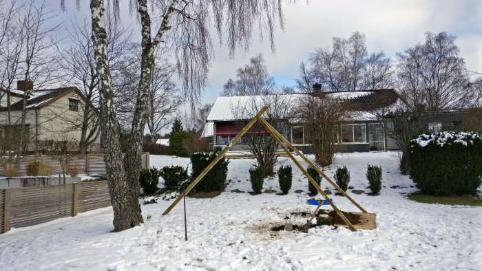 Hembyggd gungställning av trä, fastsatt i snötäckt trädgård med infästning i träd, synlig gammal gren.