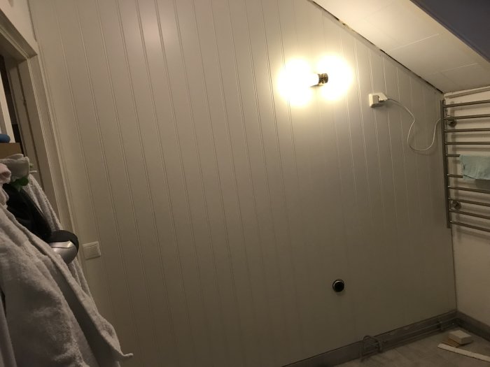 Badrum under renovering med nyuppsatt vit panel på vägg, eluttag och handdukstork.