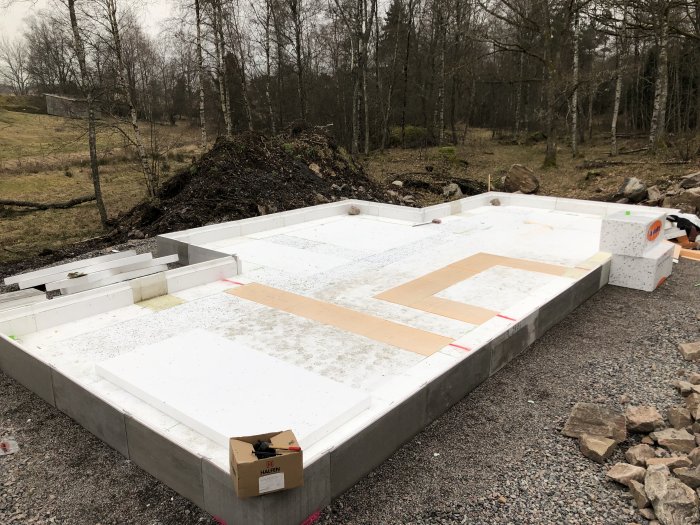 Cellplastisolering installerad på grund till byggprojekt, med natur och byggmaterial i bakgrunden.