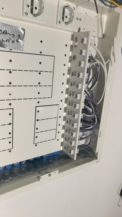 Ett öppet mediaskåp med oorganiserade nätverkskablar och Ethernet-portar.