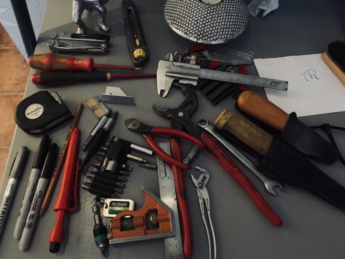 En samling verktyg inklusive elkniv, knipextång och måttband på arbetsbord redo för rengöring.