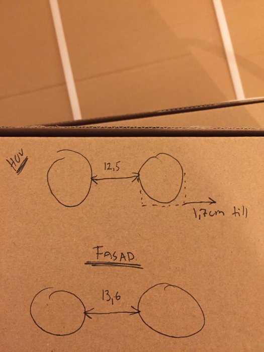 Handritad skiss visar position och mått på hål i en huvs och tegelväggs utformning, med markerade mått och justeringar.