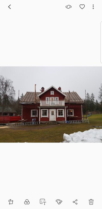 Ett rött hus med arbetare som byter tak, byggställningar och snötäckt mark.