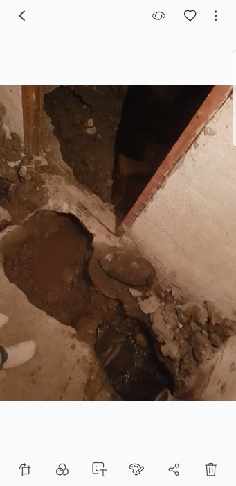 Uppgrävd golvyta som visar ett skadat avloppsrör vid en husrenovering.