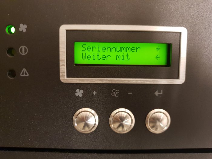 Digitalt displayfönster som visar texten "Seriennummer" och "Weiter mit" på tyska med styrknappar på en apparat.