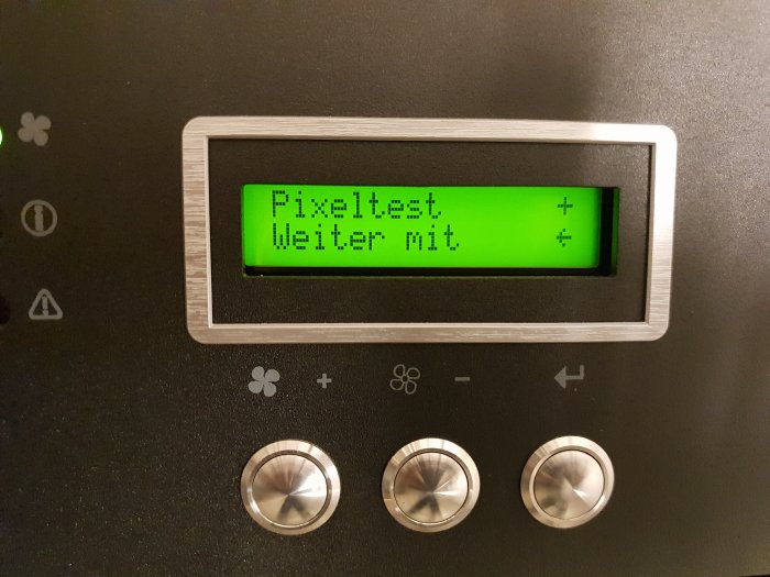 Display på en apparat med texten "Pixeltest Weiter mit" och omgivande kontrollknappar.