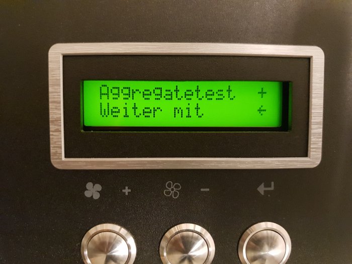 Digital kontrollpanel med tysk text "Aggregat testet" och "Warte nit" på en grön monokrom skärm.