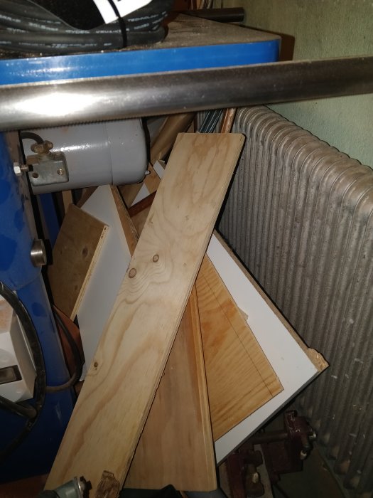 Oorganiserad samling av plywoodbitar lutade mot en arbetsbänk och radiator i en verkstad.