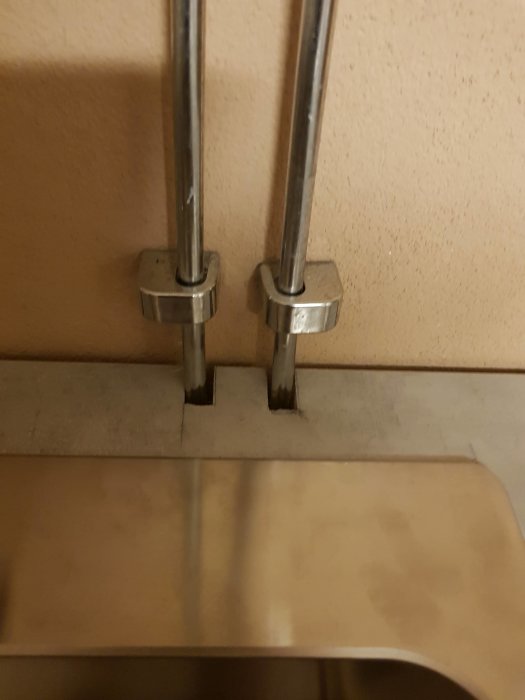 Vattenledningsrör i metall installerade under en vask med ett synligt hack i kanten på den bruna skivan.