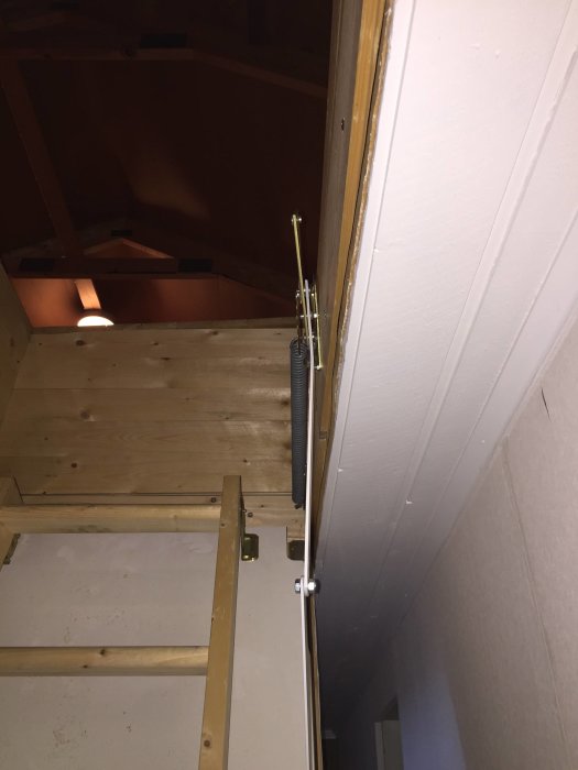 En skadad vindstrappa med böjda metallarmar och sprucket trä där fjädrar är fästa i ett äldre hus.