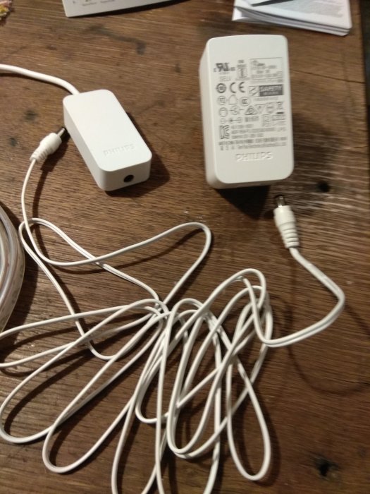 Philips varumärkesladdar och adapter med instruktionsikoner på en trasslig vit kabel på ett träbord.