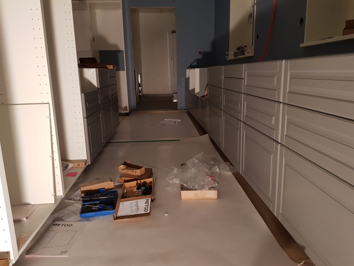 Kök under renovering med omonterade skåpsluckor och utspridda verktyg och byggmaterial.