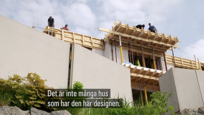 Arbetare bygger träkonstruktion på ett hus under konstruktion med ovanlig design.