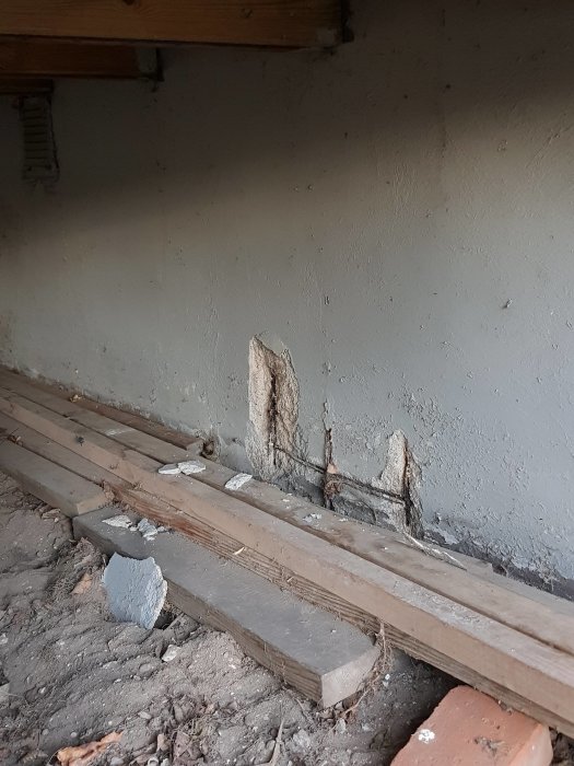 Bild på grund med synlig armering och rostsprängning, målad yta och träbrädor framför.