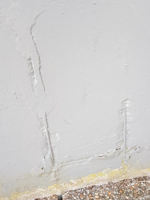 Grund med synlig armering och rostsprängningar, delvis övermålad vägg.