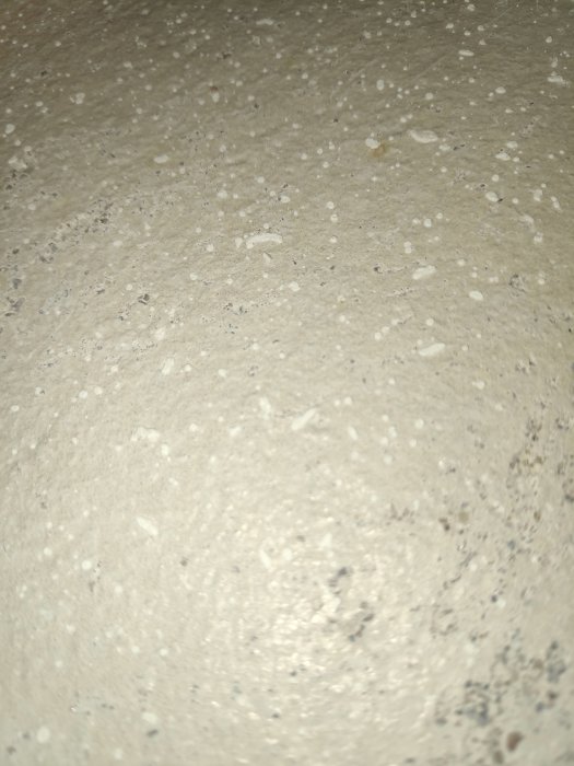 Närbild på en betongyta med små, vita, porösa prickar som inte löses upp i vatten.
