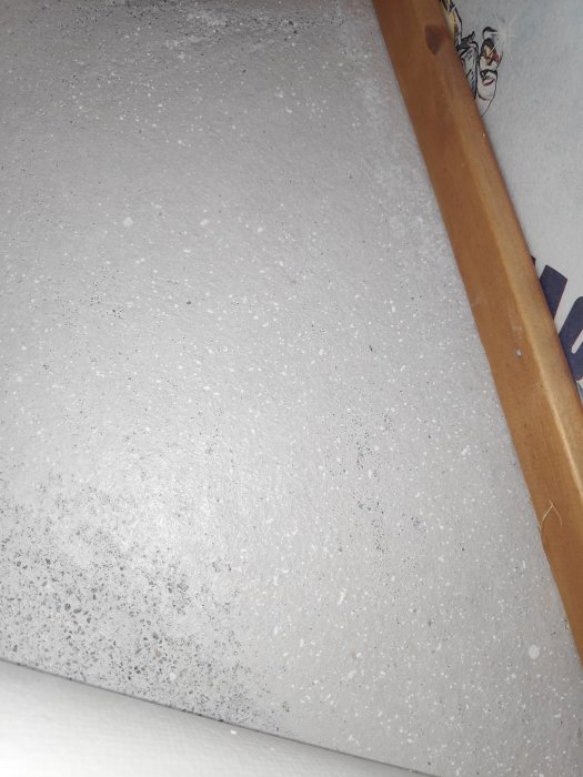 Betonggolv med oregelbundna vita prickar nära en trälist, eventuell kalkavlagring, inga fuktfläckar synliga.