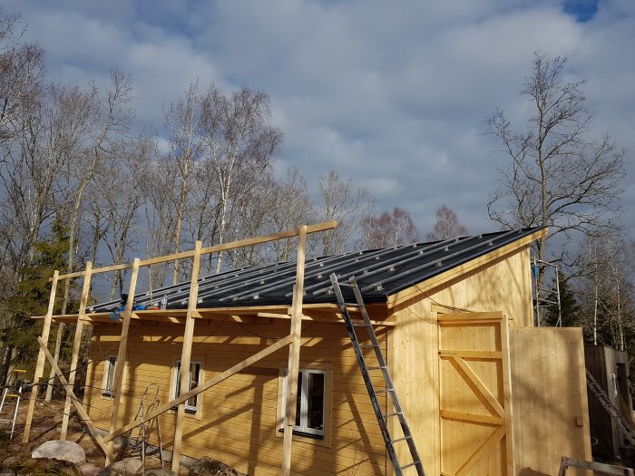 Solcellspaneler installerade på ett garage med en trästege och en byggställning runt byggnaden under en delvis molnig himmel.