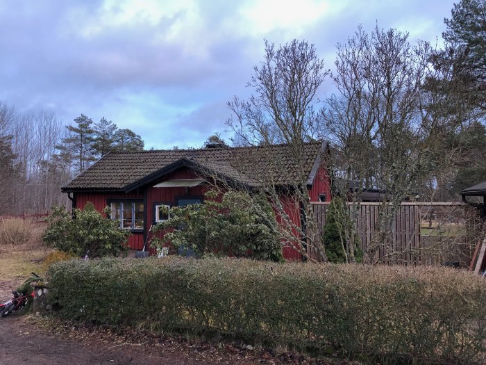 Rödmålat hus med komplex takkonstruktion, oordnad baksida och leksaker på marken.