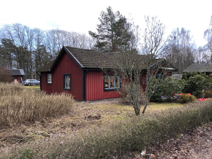 Rött trähus med varierad takkonstruktion, oorganiserade föremål på altanen.