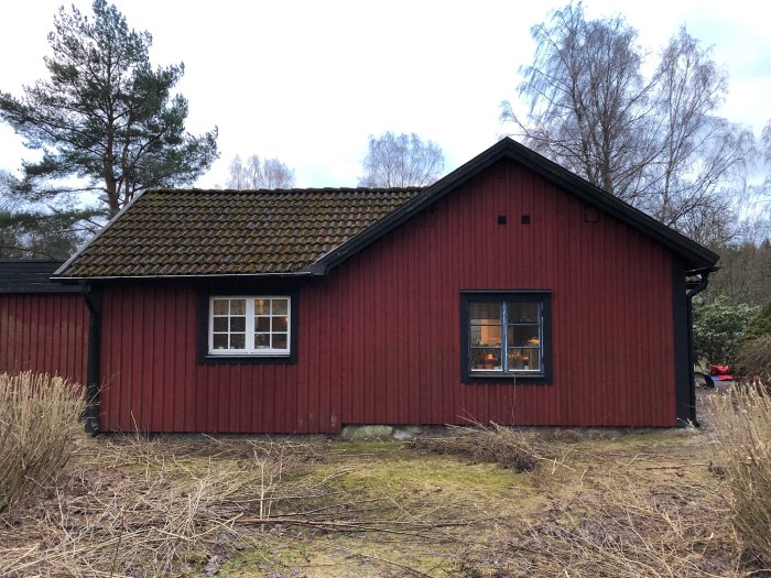 Rött hus med mossbelagt tak och oordnad baksida som visar tecken på renoveringsprojekt.