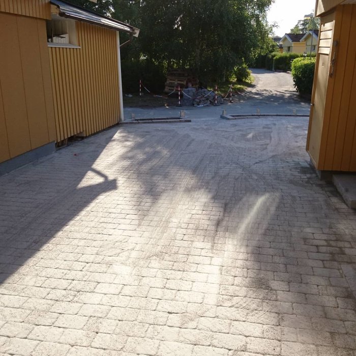 Nybelagd uppfart av stenplattor vid en gulfärgad byggnad med arbetsmaterial i bakgrunden.