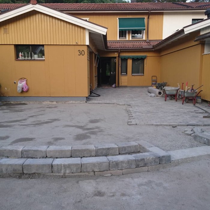 Framsidan av ett gult hus med en delvis färdigställd stengång och trappa utan stenar.