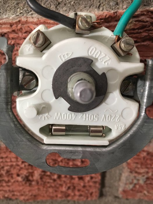 Närbild av en demonterad vit strömbrytare eller dimmer visar ledningar och skruvanslutningar mot en tegelväggsbakgrund.