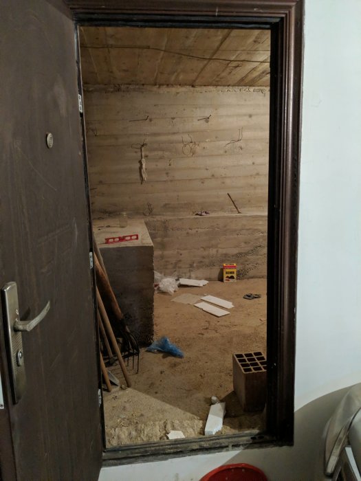 Upprensad men ostädad förrådsutrymme med tomma väggar och sparsamma föremål på golvet, redo för renovering.