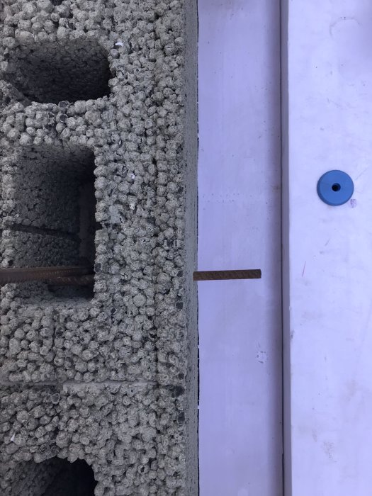 Armeringsjärn sticker ut från hål i en murblocksvägg bredvid en nygjuten vit betongplatta.
