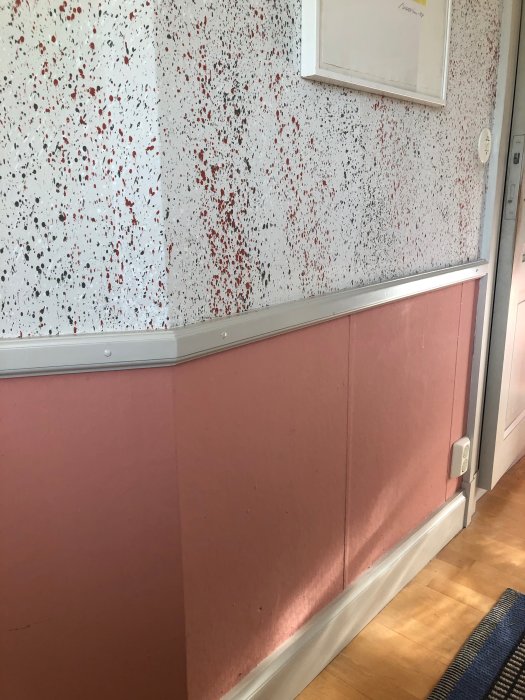 Vägg med stänkmålning i rött och svart över rosa lumppapp, grundmålad med linoljefärg.
