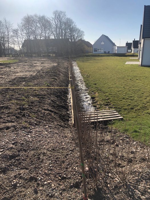 Nygrävd slänt närmre tomtgräns med förflyttad häck och staket, mot bakgrund av bostadsområde.