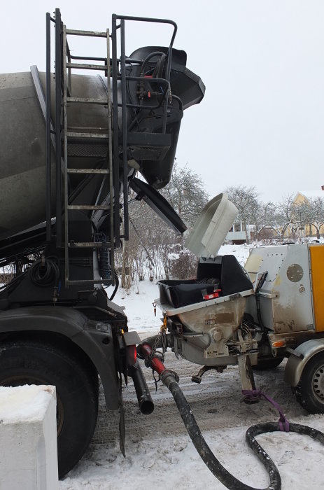 En betongbil pumpar självkompakterande betong på en vinterdag, vilket är ett steg i renoveringen av ett källargolv.