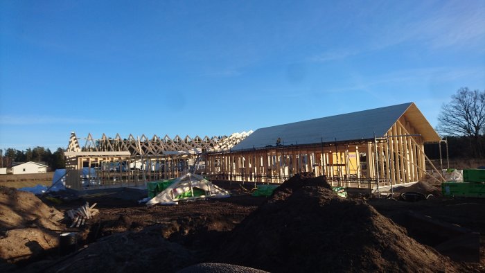 Konstruktion av hus med pågående råspontarbete, synliga takstolar och blå himmel.