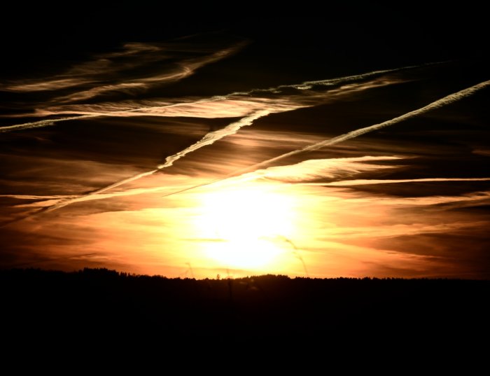 Dramatisk solnedgång med moln och kondensstrimmor på himlen.