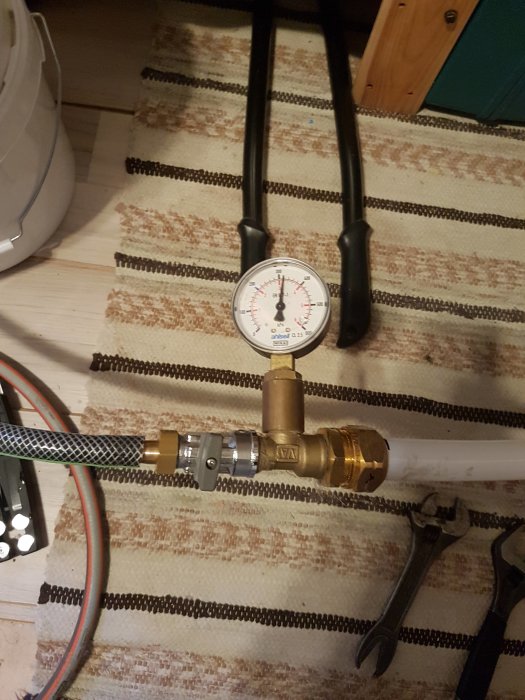 Golvvärmeinstallation med manometer som visar tryck, kopplad till PEX-rör och ventiler.