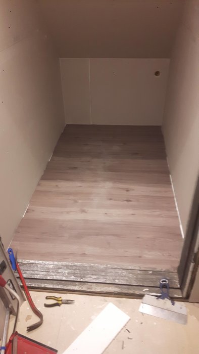 Renoverat förrådsutrymme under trappa med nytt vinylklick golv och verktyg på golvet.