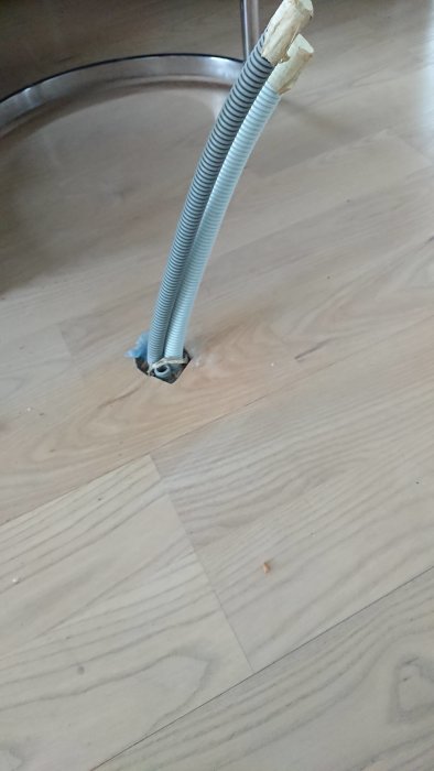 Flexrör som sticker upp ur ett trägolv, avsett för el och media, oklart hur det ska användas.