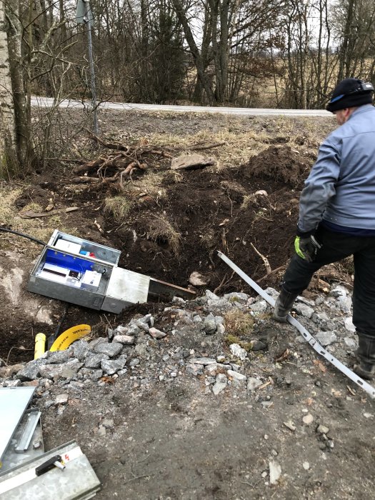 Armering för kantbalk och öppet markskåp vid byggplats med en person och kabelrör synliga.