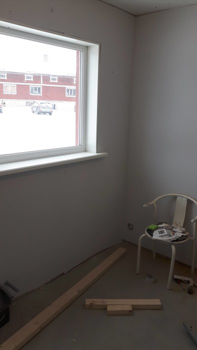 Renoveringsrum med ett nyinstallerat fönster, väggar målade i grått och träreglar på golvet.