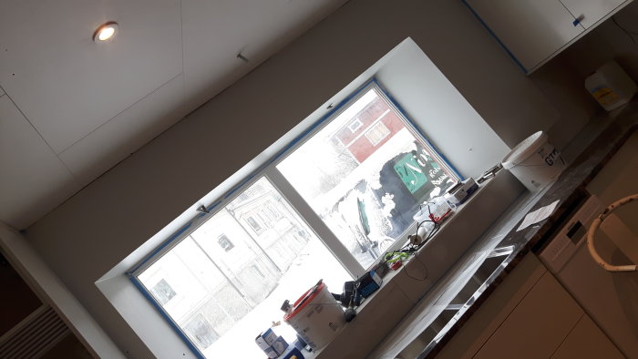 Renoverat kök med rörslingor och säckar på bänk, ny fönsterbänk, tejpade rör och snickerier.