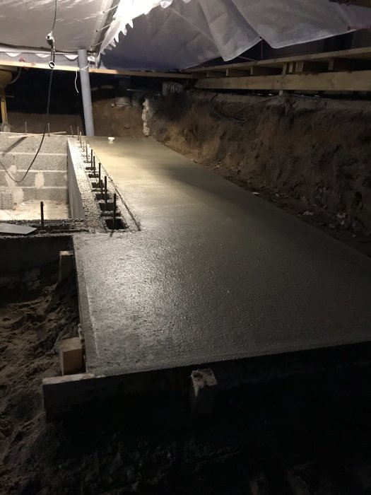 Nyutgjuten betongplatta under hus med formar och armeringsjärn i belysning.