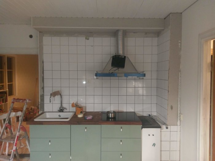 Kök under renovering med halvfärdig målningsarbete och provisorisk köksfläktinstallation.