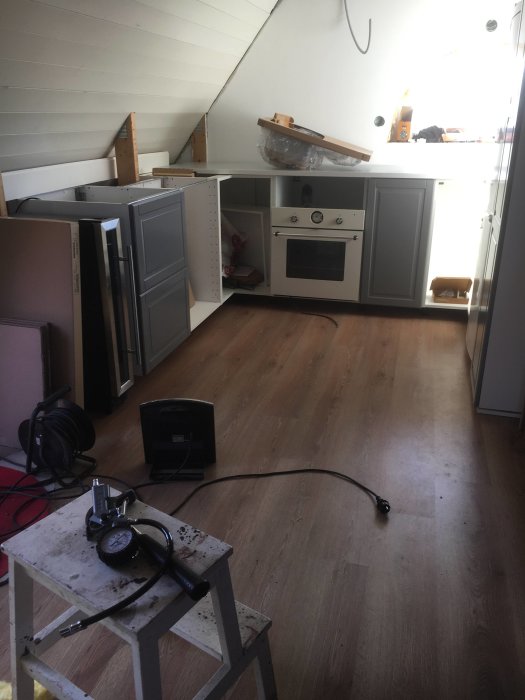 Omonterade köksskåp och vitvaror i ett rum under renovering med verktyg och byggmaterial utspridda på golvet.