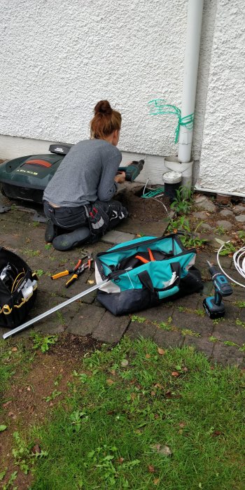 Person installerar fiberkabel vid en husvägg bredvid en verktygsväska och elverktyg.