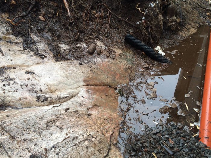 Oavslutat dräneringsarbete med synligt rör som går in i grunden, vatten och upprivet mark.
