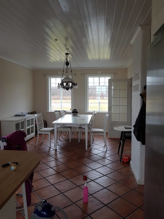 Ett ljust kök med vita möbler, klinkergolv och utspridda föremål som tyder på renovering.